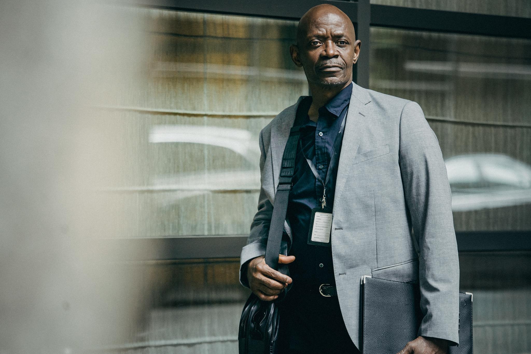 Concentrated African American businessman in formal suit standing with laptop bag and folder against tiled wall in metro station